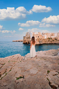 Woman standing on rock by sea against sky