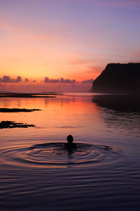 Silhouette man in sea against sky during sunset