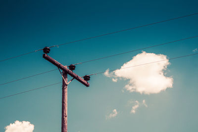 Low angle view of bird perching on electricity pylon against blue sky