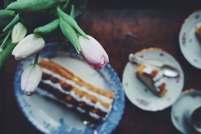 High angle view of cream cake in plates and tulips on table