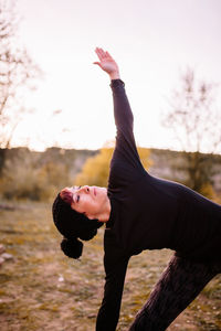 Woman stretching at park against sky