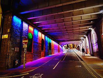 Rear view of man walking in illuminated multi colored tunnel