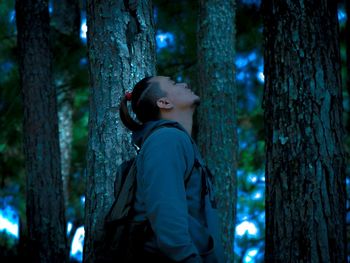 Side view of man standing by tree trunk in forest