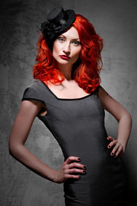 Portrait of young redhead woman with hands on hip standing against wall