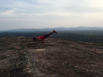 Side view of man practicing handstand on rock formation against sky