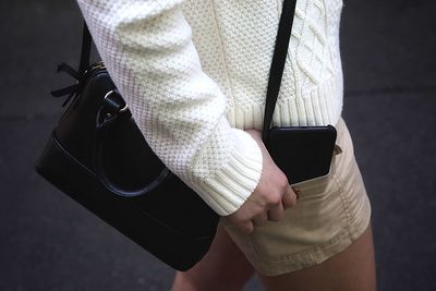 Midsection of woman with mobile phone in pocket standing on street