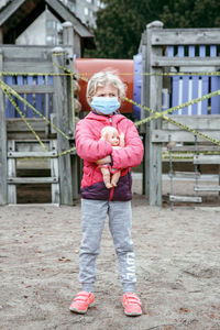 Girl wearing mask holding doll while standing at beach