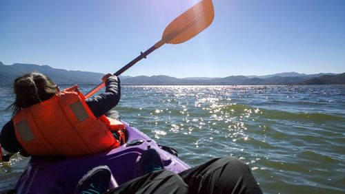 Rear view of woman canoeing on sea against sky during sunny day