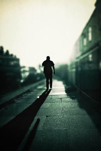 Rear view of silhouette man walking on sidewalk against clear sky