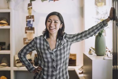 Happy female clerk standing with hand on hip at fashion store