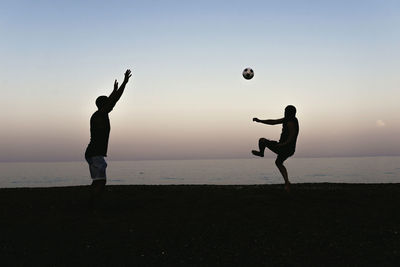 People playing soccer on beach against sky during sunset