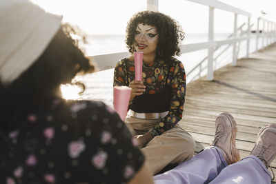 Teenage girl looking at female friend while sitting on pier