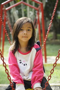 Portrait of girl sitting on swing in playground