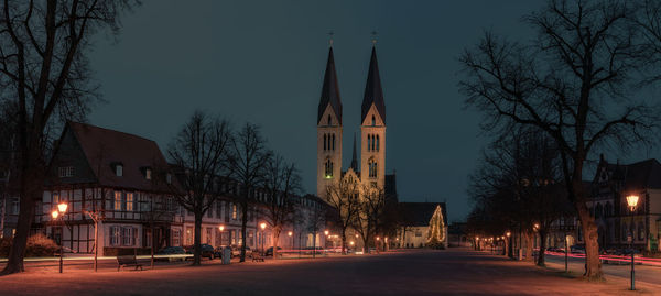 Illuminated street amidst buildings against sky at night