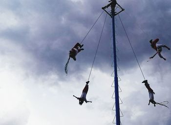 Low angle view of men flying hanging against sky