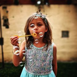 Cute girl blowing bubbles while standing outdoors