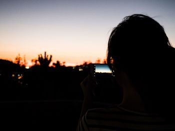 Silhouette of woman photographing camera at sunset