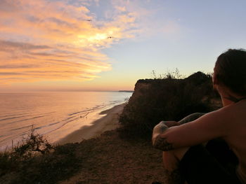 Midsection of woman sitting on beach against sky during sunset