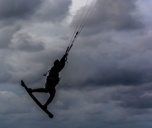 Silhouette person kiteboarding against cloudy sky at dusk