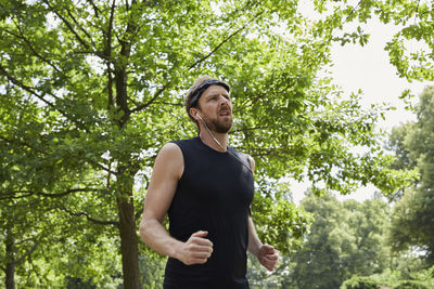 Man listening music while running against trees in park