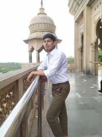 Portrait of young man standing by railing against building