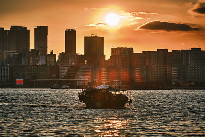 Sea by buildings against sky during sunset