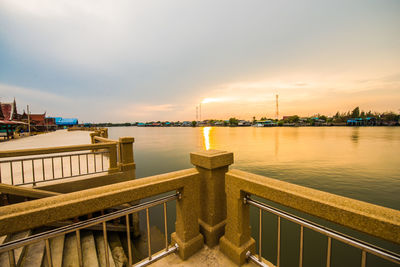 Illuminated city by sea against sky during sunset