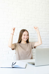Portrait of smiling young woman using mobile phone against wall