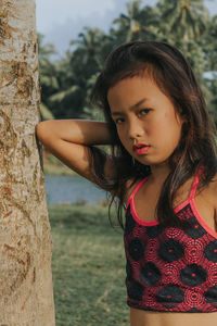 Portrait of a beautiful young woman standing against tree trunk