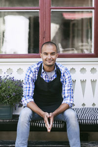 Portrait of smiling man sitting on bench against window