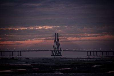 Suspension bridge over sea against sky during sunset