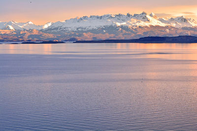 Scenic view of sea by snowcapped mountains against sky during sunset