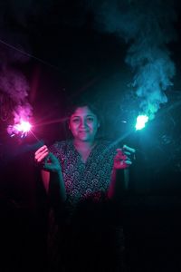 Portrait of smiling young woman holding sparklers at night