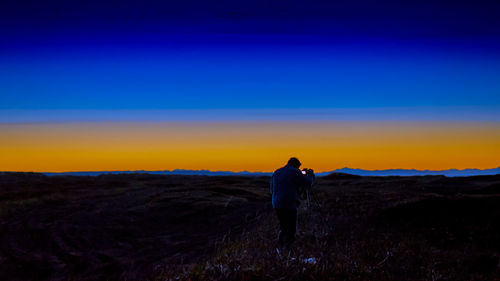 Rear view of silhouette man standing on field against sky at sunset