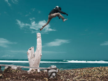 Man jumping at sea shore against sky