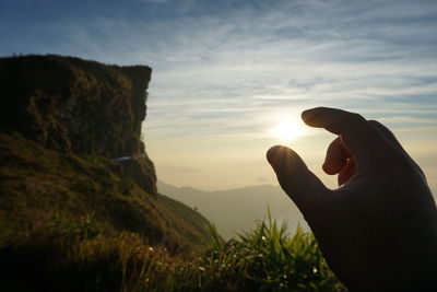 Optical illusion of person holding sun against sky during sunset