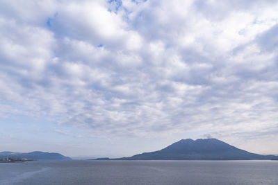 Scenic view of sea by mountain against sky