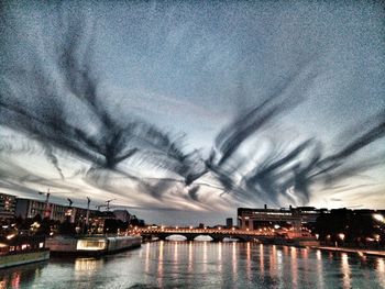 River by illuminated city against cloudy sky