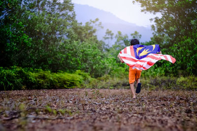 Rear view of boy holding malaysian flag while running on field