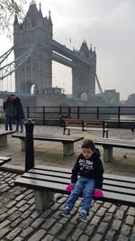 Woman sitting on bridge against sky in city