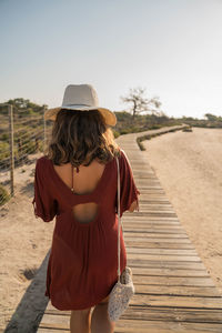 Rear view of woman standing on boardwalk against clear sky