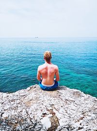 Rear view of shirtless man looking at sea against sky