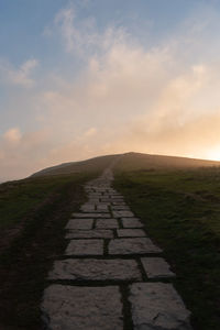 Footpath amidst field against sky during sunset