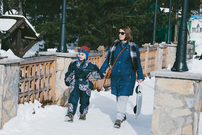 Full length of mother and son holding hands while walking on road during winter