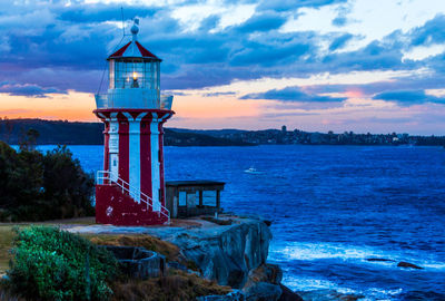 Lighthouse by sea against sky during sunset