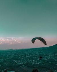 Person paragliding over sea against sky