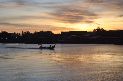 Silhouette boat in river against sky during sunset