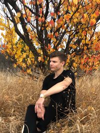 Woman looking away while standing by tree during autumn