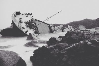 View of a sinking ship in water with rocks in foreground