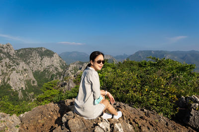 Portrait of young woman sitting on mountain against sky